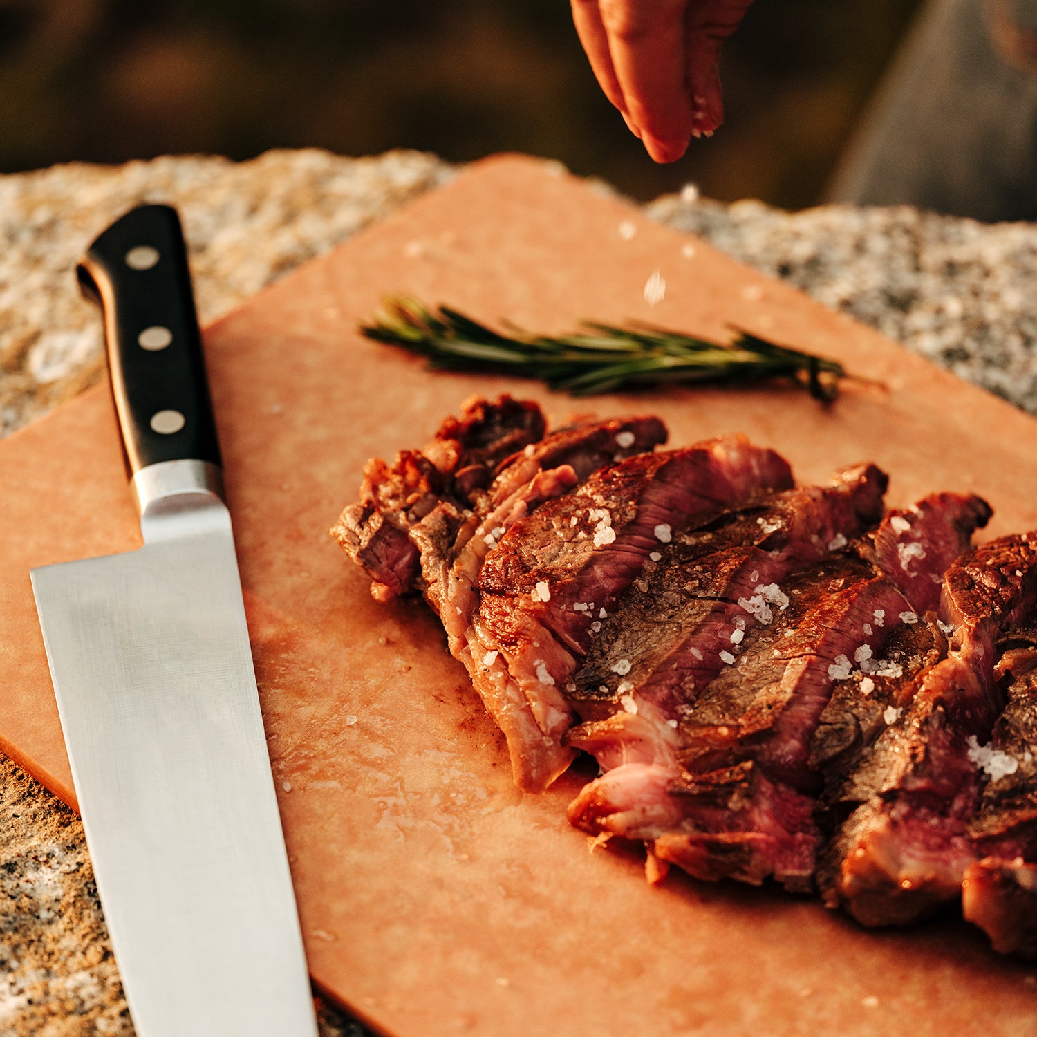 Sliced roasted meat on a wooden cutting board with rosemary being garnished with Celtic Sea Salt